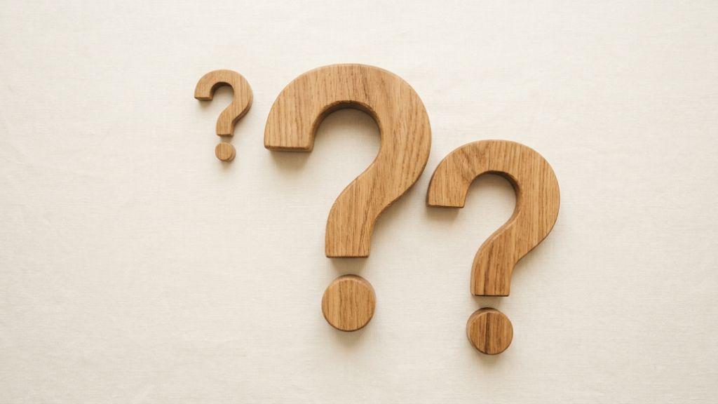 木製の「?」マークのオブジェクトが並ぶ、疑問を象徴するミニマルな俯瞰カット.jpg